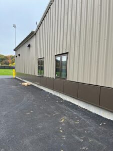 Sidelong view of the vertically paneled Transportation garage with an athletic field and lights visible in the background