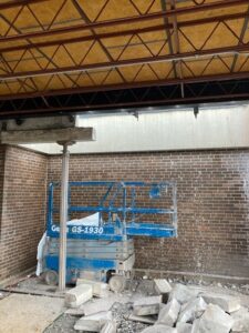 A large blue lift sits amid concrete rubble against a brick wall exterior.